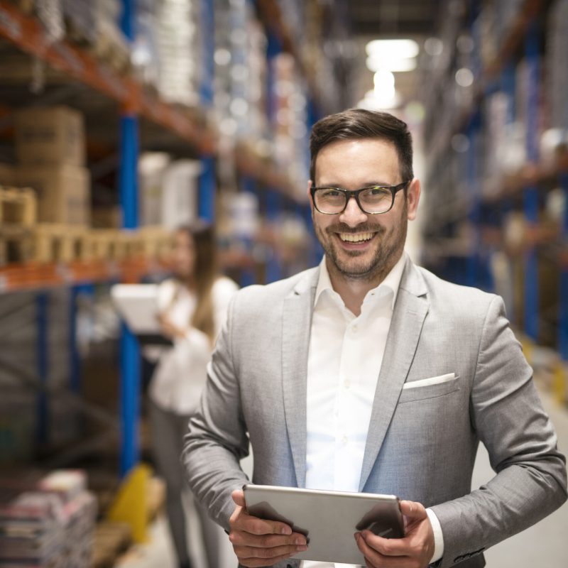 Portrait of successful middle aged caucasian manager businessman holding tablet computer in large warehouse organizing distribution.